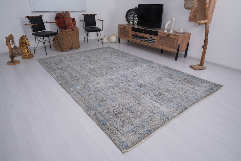 May include: A light blue and gray patterned rug with a faded, vintage look. The rug is laid out on a white wood floor in a living room setting.
