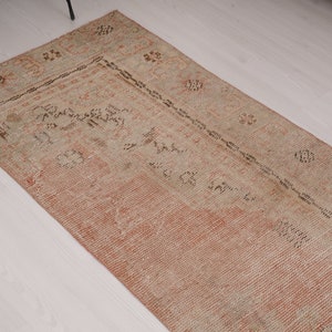 May include: A vintage runner rug with a faded pink and beige color scheme. The rug has a traditional Persian design with intricate floral patterns and a central medallion.