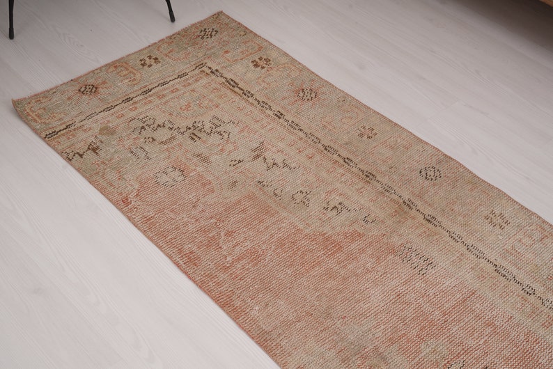 May include: A vintage runner rug with a faded pink and beige color scheme. The rug has a traditional Persian design with intricate floral patterns and a central medallion.