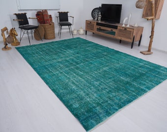May include: A teal blue vintage rug with a distressed look. The rug is laid out on a white wood floor in a room with furniture.