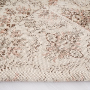 Peut inclure: Gros plan sur un tapis cr&egrave;me avec un motif floral d&eacute;licat dans des tons de brun et de rose. Le tapis a une texture tiss&eacute;e et un aspect l&eacute;g&egrave;rement vieilli.