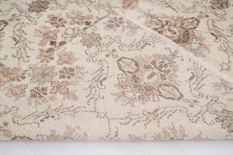 Peut inclure: Gros plan sur un tapis cr&egrave;me avec un motif floral d&eacute;licat dans des tons de brun et de rose. Le tapis a une texture tiss&eacute;e et un aspect l&eacute;g&egrave;rement vieilli.