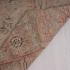 May include: Close-up of a beige and brown woven rug with a pink fringe. The rug is folded in half, revealing the underside.