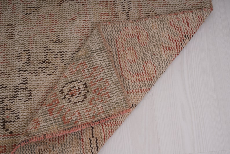 May include: Close-up of a beige and brown woven rug with a pink fringe. The rug is folded in half, revealing the underside.