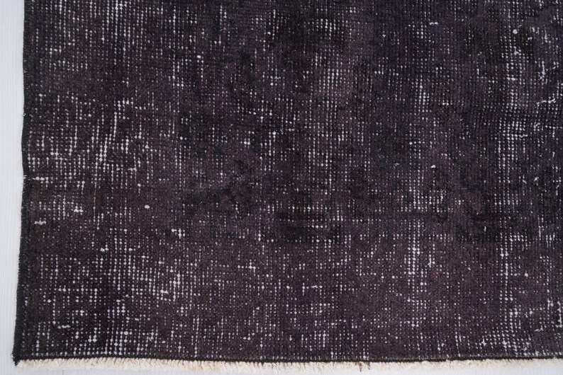 Puede incluir: Primer plano de una alfombra oscura y desgastada con una superficie texturizada. La alfombra tiene una combinaci&oacute;n de colores negro y gris con reflejos blancos, creando una apariencia vintage o antigua. Los bordes est&aacute;n deshilachados.