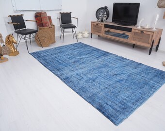 May include: A blue distressed rug with a subtle pattern, laid out on a white wood floor in a living room setting. The rug is in front of a wooden entertainment center with a television and decorative items.