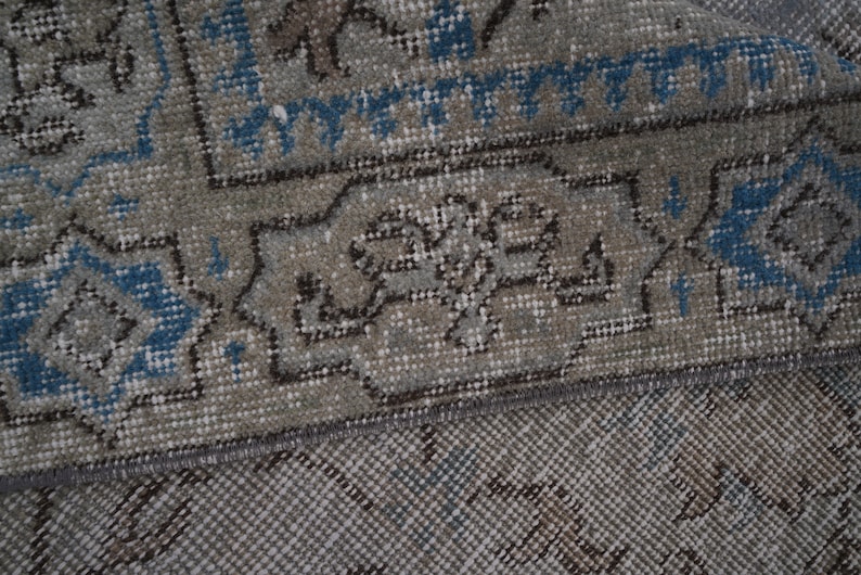 May include: Close-up of a gray and blue patterned rug with a fringe border. The rug has a traditional design with intricate details.