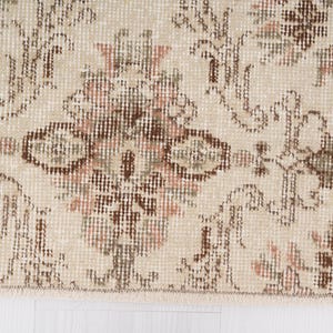 Peut inclure: Gros plan d'un tapis beige avec un motif floral dans les tons de brun et de rose. Le tapis a une bordure frang&eacute;e.