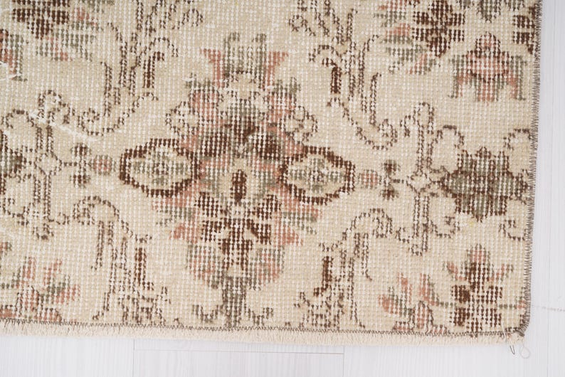 Peut inclure: Gros plan d'un tapis beige avec un motif floral dans les tons de brun et de rose. Le tapis a une bordure frang&eacute;e.
