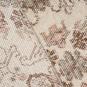 Peut inclure: Gros plan sur un tapis beige avec un motif floral brun et rose. Le tapis a une texture tiss&eacute;e et une bordure frang&eacute;e.