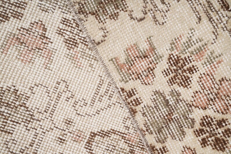 Peut inclure: Gros plan sur un tapis beige avec un motif floral brun et rose. Le tapis a une texture tiss&eacute;e et une bordure frang&eacute;e.