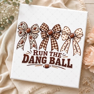 May include: A white rectangular canvas featuring three decorative bows in leopard print, brown plaid, and polka dot patterns, each centred with a brown football. Below the bows, the text reads RUN THE DANG BALL in brown letters.