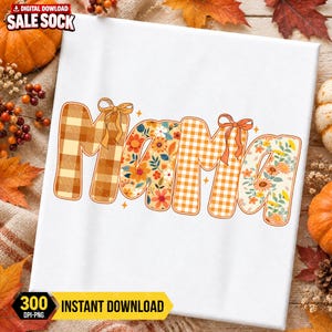 May include: A white graphic design featuring the word MAMA in a stylized font. The letters alternate between an orange and white plaid pattern and a floral print with orange, yellow, and blue flowers. Two orange bows are tied to the letters.