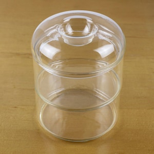 May include: A clear, three-tiered glass serving dish with a domed lid. The dish has a circular base and a cylindrical body, perfect for displaying desserts or appetizers. The glass is transparent, allowing a full view of the contents.