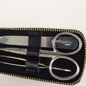 May include: A black zippered case containing a nail file, small scissors, and tweezers. The scissors have a curved blade and the text "Special Triple Cut GERMANY" is visible. The case has a gold zipper.