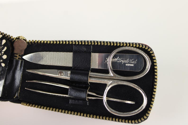 May include: A black zippered case containing a nail file, small scissors, and tweezers. The scissors have a curved blade and the text "Special Triple Cut GERMANY" is visible. The case has a gold zipper.