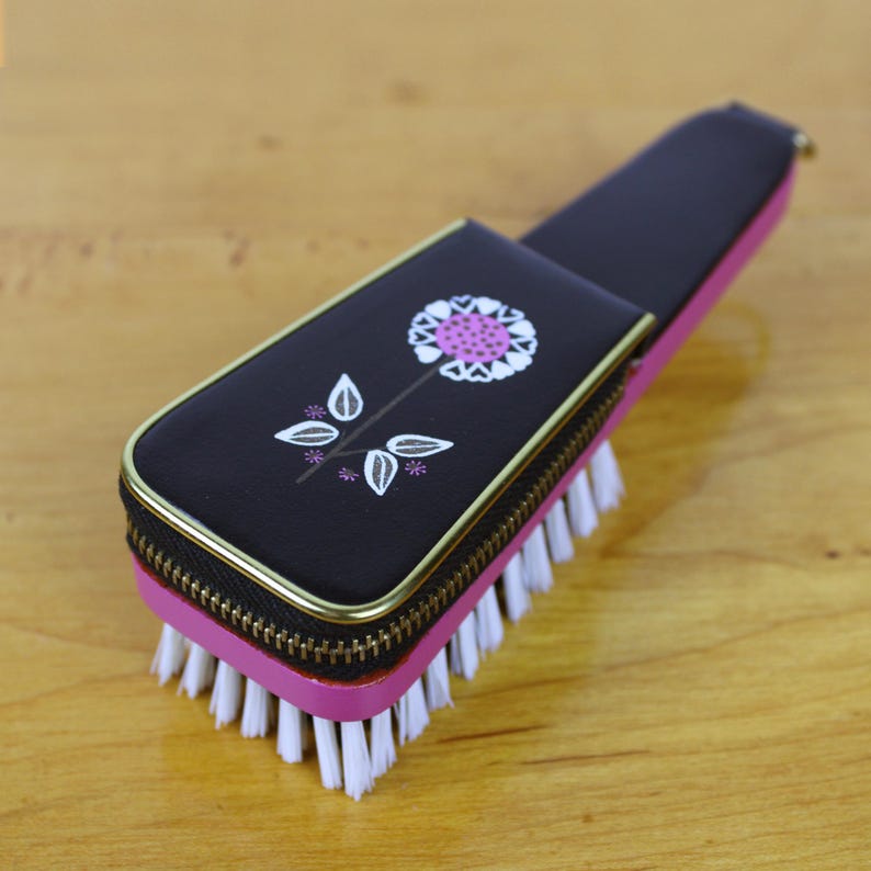 May include: A vintage black and pink brush with a floral design. The brush has a black case with a zipper and a gold trim. The floral design is white and pink. The bristles are white.