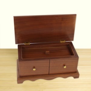 May include: A wooden jewelry box with a hinged lid and two drawers. The box is made of dark brown wood with a polished finish. The drawers have small, round gold-colored knobs. The lid is open, revealing a compartment inside.