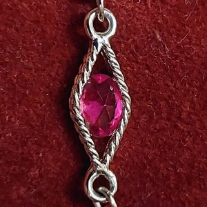 Op de afbeelding: Een zilveren armband met een roze edelsteen in een ruitvormig frame.