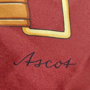 May include: A close-up of a red silk scarf with a gold buckle design and the signature "Ascot" in black script.