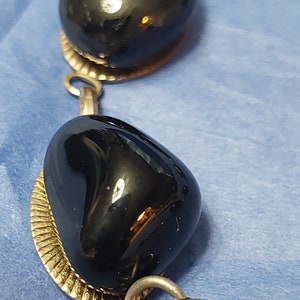 May include: A black onyx bracelet with silver links and a round silver clasp. The bracelet features three large, polished black onyx stones.