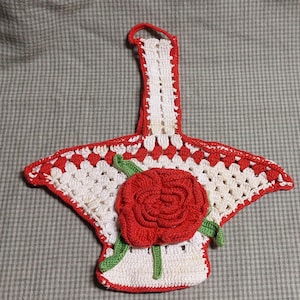 Op de afbeelding: Een witte en rode gehaakte ovenwant met een rode roos in het midden. De ovenwant heeft een lus om op te hangen.