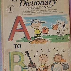 May include: The cover of a book titled "The Charlie Brown Dictionary" with a red "A" and a green "B" on the front. The book is volume 1 of an 8-volume set and features illustrations of Charlie Brown and Snoopy.