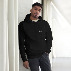 Op de afbeelding: Een zwarte hoodie met een klein wit grafisch logo op de linkerborst. De trui is voorzien van een capuchon met trekkoord, lange mouwen met geribbelde boorden en een kangoeroezak aan de voorzijde. Gedragen met een donkergrijze spijkerbroek.