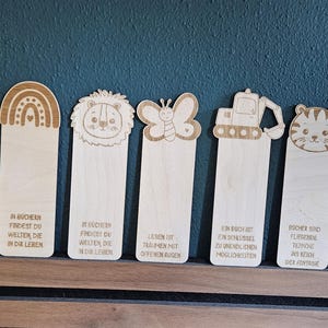 Könnte beinhalten: Eine Sammlung von Holz-Lesezeichen mit verschiedenen eingravierten Designs, darunter ein Fußball, ein Astronaut, ein Regenbogen, ein Löwe, ein Schmetterling, ein Bagger, ein Tiger, eine Blume und ein Dinosaurier. Jedes Lesezeichen hat ein einzigartiges Zitat.