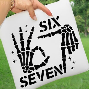 May include: White square pillow with a black skeleton hand design. The design includes the words "SIX" and "SEVEN" with a hand gesture. Four small black star shapes are also included in the design.