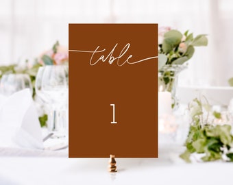 May include: A brown table number card with white calligraphy that says "table" and the number "1" in white.