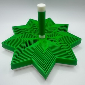 May include: A green and white star-shaped object with a green cylindrical object in the centre. The star has multiple layers of green zig-zag patterns. The cylindrical object is green with a white top.