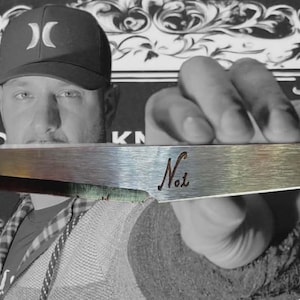 May include: A silver knife with a sharp, angled blade. The handle is engraved with the word "No.1". The background is black and white with a floral design.