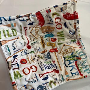 May include: White quilted pot holder with a nautical theme. The fabric is covered with images of boats, paddles, and signs with phrases like "Go Camp" and "I'd rather be fishing." The pot holder has a square shape.