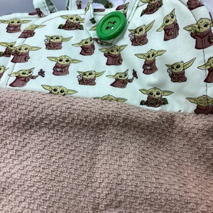 May include: A light green and brown towel with a repeating pattern of a cartoon character. The towel has a brown, textured bottom half and a top half with the character print. A large green button is visible.