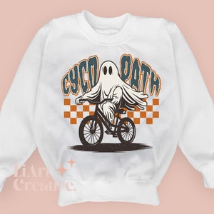 Peut inclure: Sweat-shirt blanc avec un motif d'un fant&ocirc;me &agrave; v&eacute;lo. Le fant&ocirc;me est drap&eacute; d'un drap. Le texte "CYCO PATH" est &eacute;crit dans un style r&eacute;tro. Un motif &agrave; carreaux orange et blanc est derri&egrave;re le fant&ocirc;me.