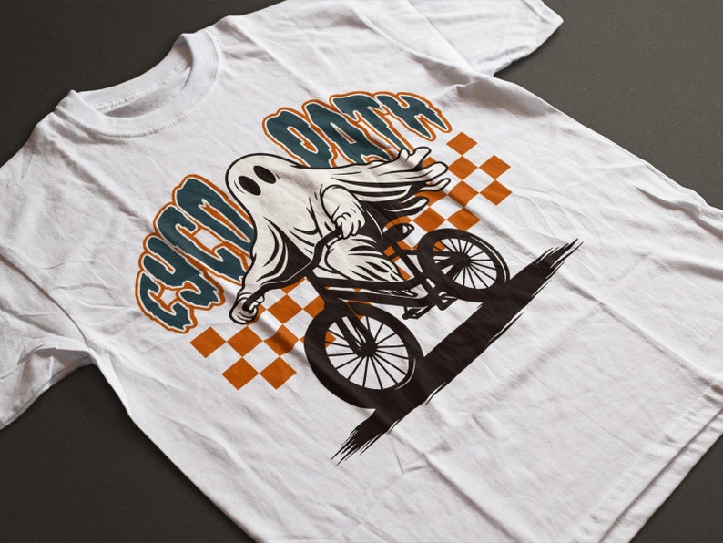 Peut inclure: T-shirt blanc avec un dessin d'un fant&ocirc;me de dessin anim&eacute; &agrave; v&eacute;lo. Le fant&ocirc;me est blanc avec des yeux noirs, faisant du v&eacute;lo noir. Le texte "CYCO OATH" est au-dessus du fant&ocirc;me en bleu sarcelle et orange. Un motif &agrave; carreaux est en arri&egrave;re-plan.