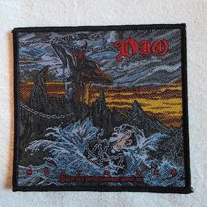 May include: A square embroidered patch featuring the Dio Holy Diver album artwork. The design depicts a figure in chains amidst turbulent blue water, rocky cliffs, and a golden sunset. The text DIO and HOLY DIVER appear in red lettering.