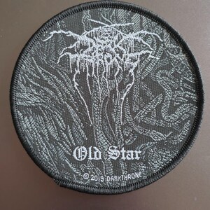 May include: A circular embroidered patch featuring a dark gray and black woven design with a stylized, jagged logo at the top. The text "Old Star" is centered below the logo, with "© 2019 DARKTHRONE" printed in small white letters at the bottom edge.