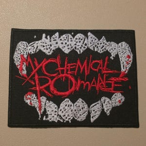 Könnte beinhalten: Ein rechteckiger, schwarz bestickter Aufnäher mit einem weißen Vampirgebiss mit roten Akzenten. Der Text "MY CHEMICAL ROMANCE" ist in rotem Garn über die Mitte der Fangzähne gestickt und weist eine gezackte, stilisierte Schriftart auf.