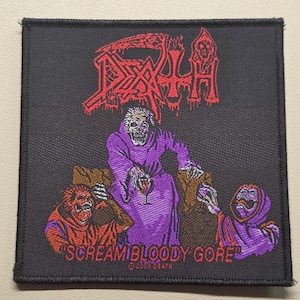 Op de afbeelding: Een vierkante zwarte geborduurde patch met het rode Death-logo bovenaan. Daaronder zit een centrale skeletfiguur in een paars gewaad tussen twee kleinere figuren, met de tekst "SCREAM BLOODY GORE" en "2009 DEATH" in het rood onderaan.