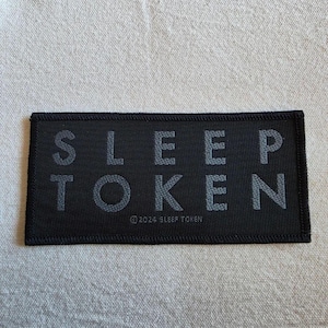 May include: A rectangular black embroidered patch featuring the text SLEEP TOKEN in a bold, dark gray sans-serif font. Below the main text, smaller text reads © 2024 SLEEP TOKEN. The patch has a thick, stitched black border.