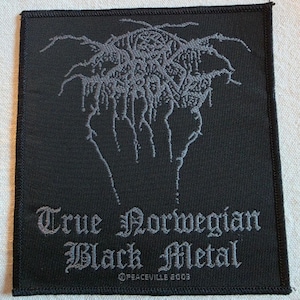 May include: A rectangular black fabric patch with a stitched border. The center features a grey, intricate, illegible logo design. Below the logo, the text reads True Norwegian Black Metal in a gothic font, with Peaceville 2003 printed below.