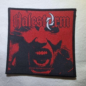 May include: A square embroidered patch featuring a red and black graphic of a face with an open mouth. The text Halestorm is printed in a stylised font at the top, with a white crescent symbol. The text 2024 WARNER MUSIC GROUP is at the bottom.