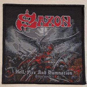 May include: A square embroidered patch featuring the red and grey Saxon logo at the top. The centre depicts a grey winged figure holding a shield with a red cross. The text Hell, Fire And Damnation and ©2024 SAXON is printed at the bottom.