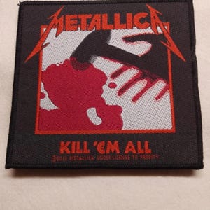 May include: A square embroidered patch featuring the Metallica logo in red at the top. The central graphic depicts a black hammer striking a red shape on a white background. The text KILL 'EM ALL appears in red below, with copyright text.