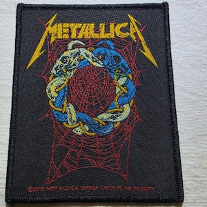 May include: A rectangular black embroidered patch featuring the yellow Metallica logo at the top. The centre displays a circular design of two intertwined snakes in blue and white over a red spiderweb pattern. Text at the bottom reads 2019 Metallica.