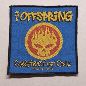 May include: A square embroidered patch with a blue background and a black border. It features the yellow text THE OFFSPRING at the top and CONSPIRACY OF ONE at the bottom. In the centre is a yellow flaming skull icon on a red circular background.