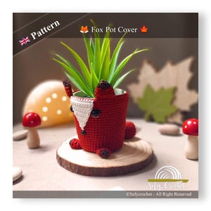 Może przedstawiać: Hakowana osłonka na doniczkę w kształcie lisa w kolorze czerwonym i białym, z zieloną rośliną w środku. Osłonka na doniczkę jest umieszczona na drewnianym plastrze.