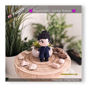 May include: Crocheted amigurumi figure of a character from the anime Jujutsu Kaisen. The figure is wearing a black jumpsuit and has black hair. The figure is standing on a wooden surface with a small potted plant in the background.